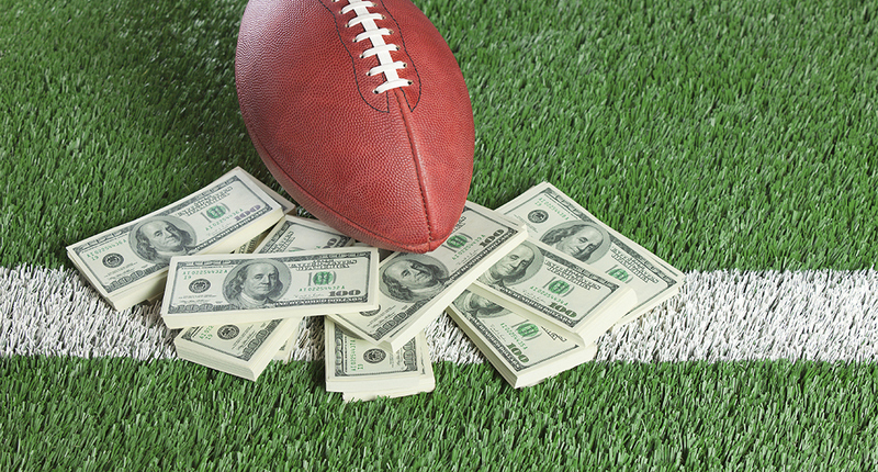 An NFL football sits with a pile of money on a green field